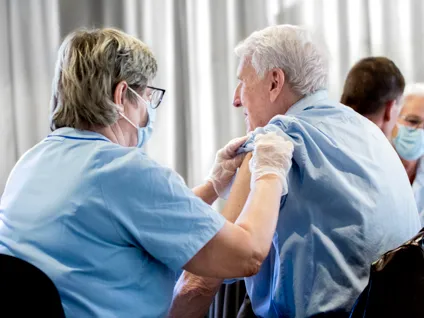 Sjuksköterska Ylva kavlar upp ärmen på en äldre man inför en vaccination.