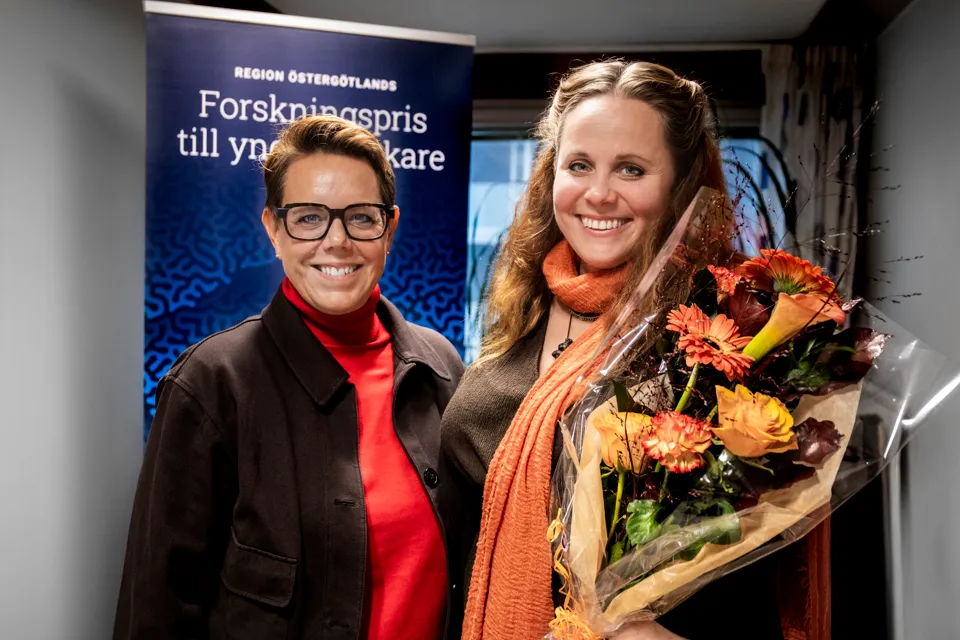 Två glada kvinnor som står bredvid varandra. Den ena håller en bukett blommor.